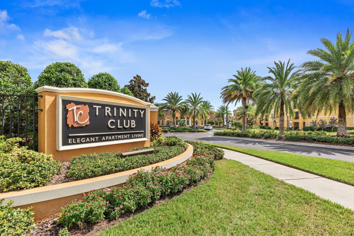 Trinity Club Monument Sign in front of driveway with palm trees
